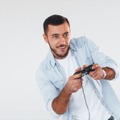 Holds joystick in hands. Young handsome man standing indoors against white background Free Photo