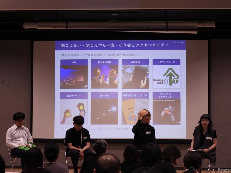 4人の登壇者が並んで座るパネルディスカッションの様子。背後のスクリーンには『聞こえない・聞こえづらい方・ろう者とアクセシビリティ』に関するスライドが投影され、手前には観客の姿が見える