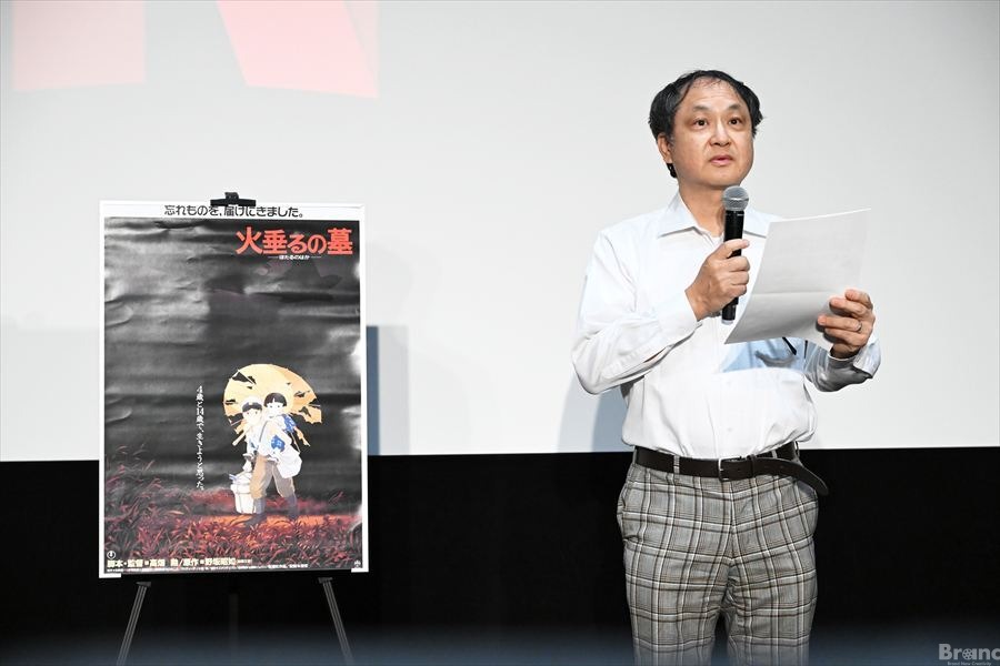 映画『火垂るの墓』のポスターが立てられたステージで、マイクと紙を持ち挨拶する新潮社の矢代新一郎氏。